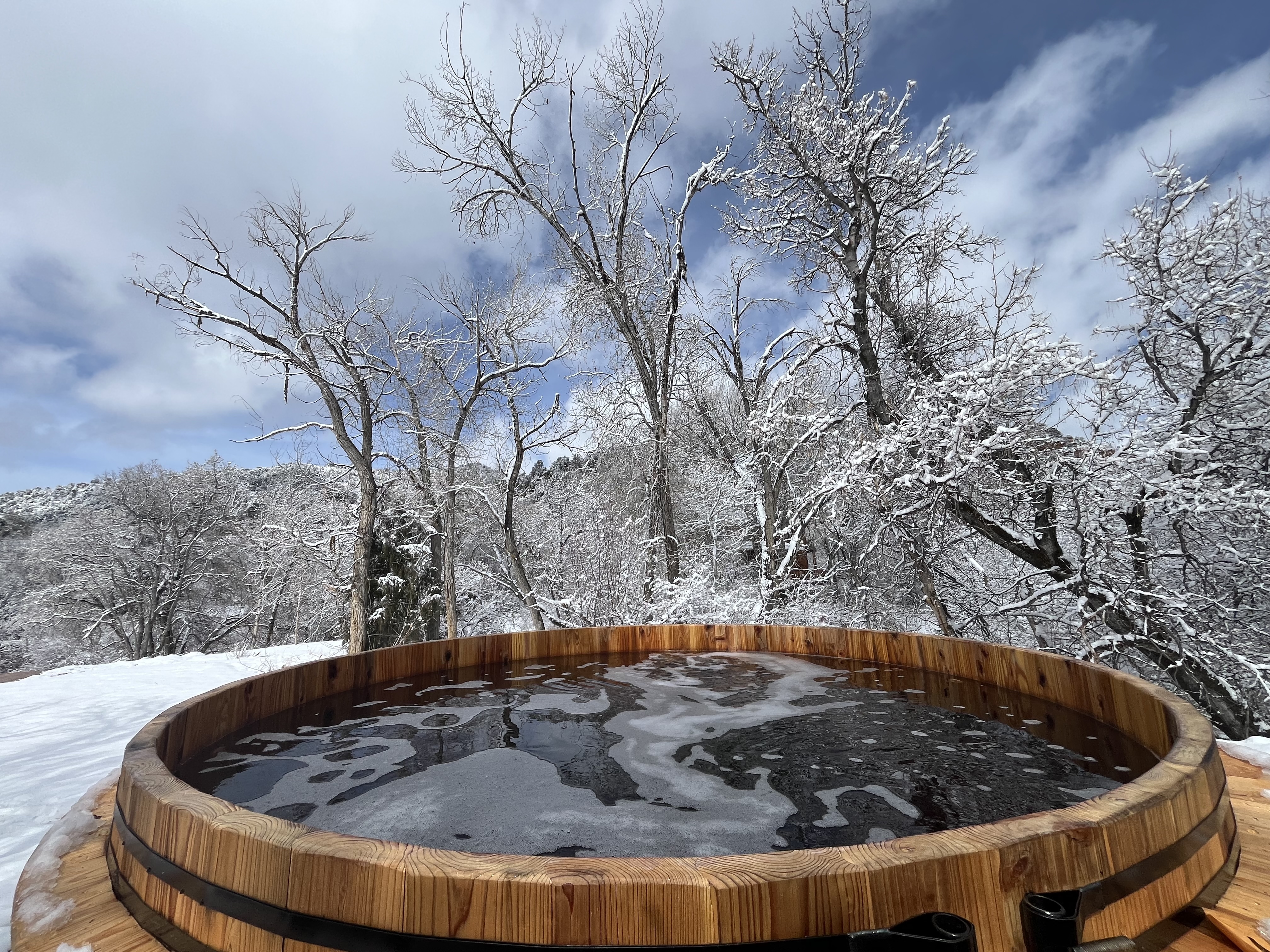 Cedar barrel hot tub surrounded by snow-covered trees at Zen Zion in winter