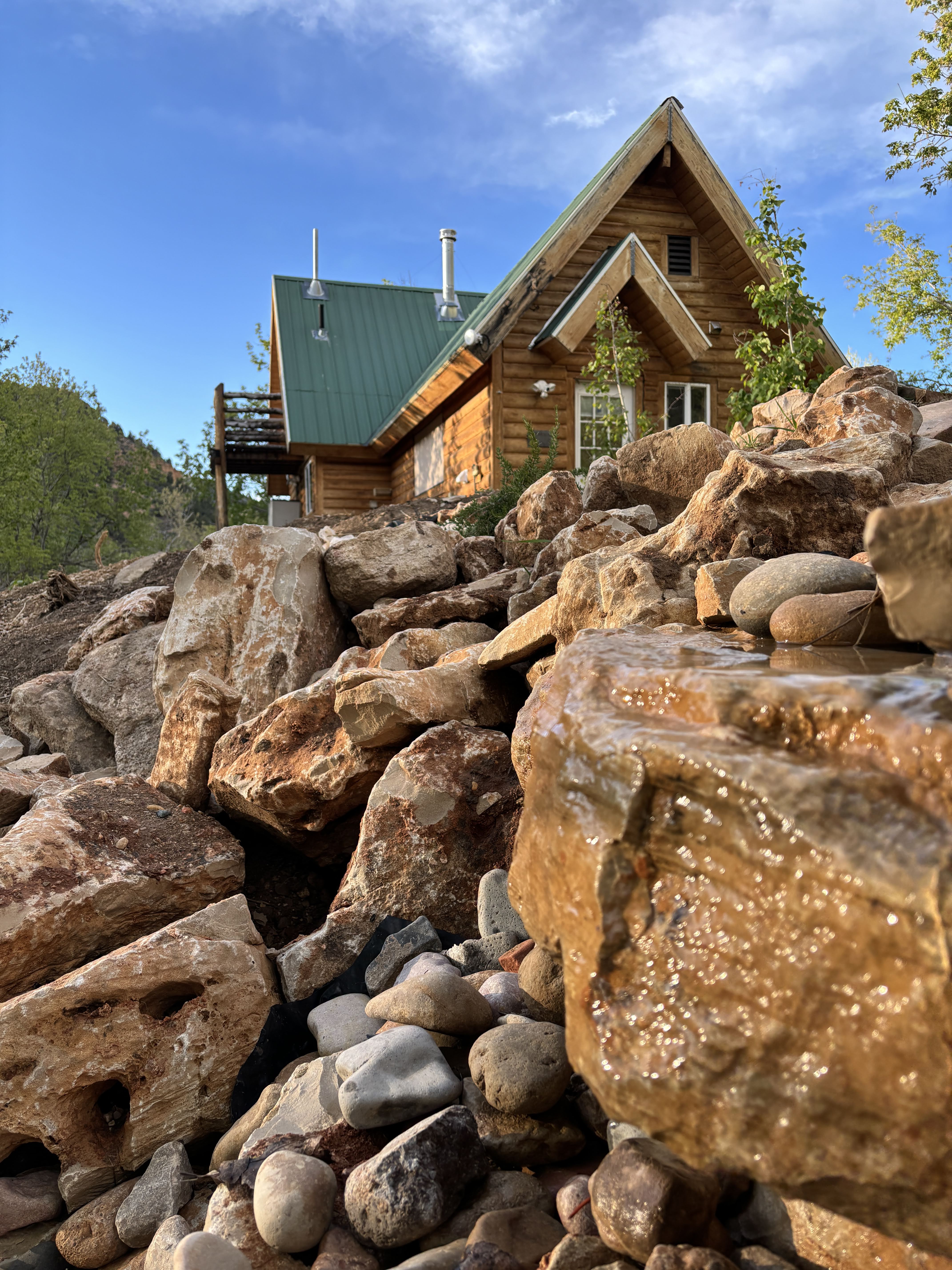 Hummingbird Cabin — log cabin with green roof perched above rocky canyon landscape at Zen Zion