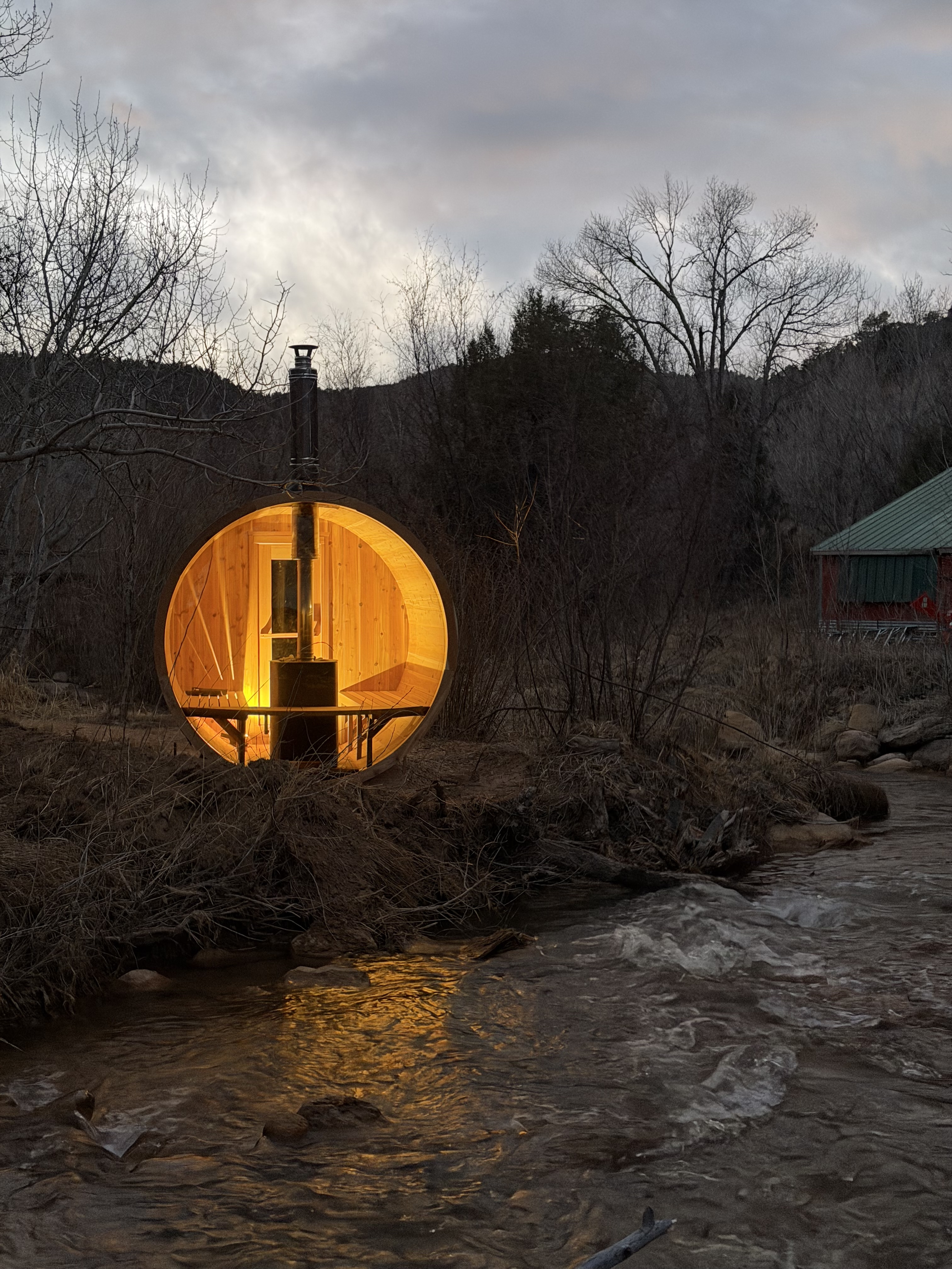 Barrel sauna glowing at dusk beside the private river at Zen Zion