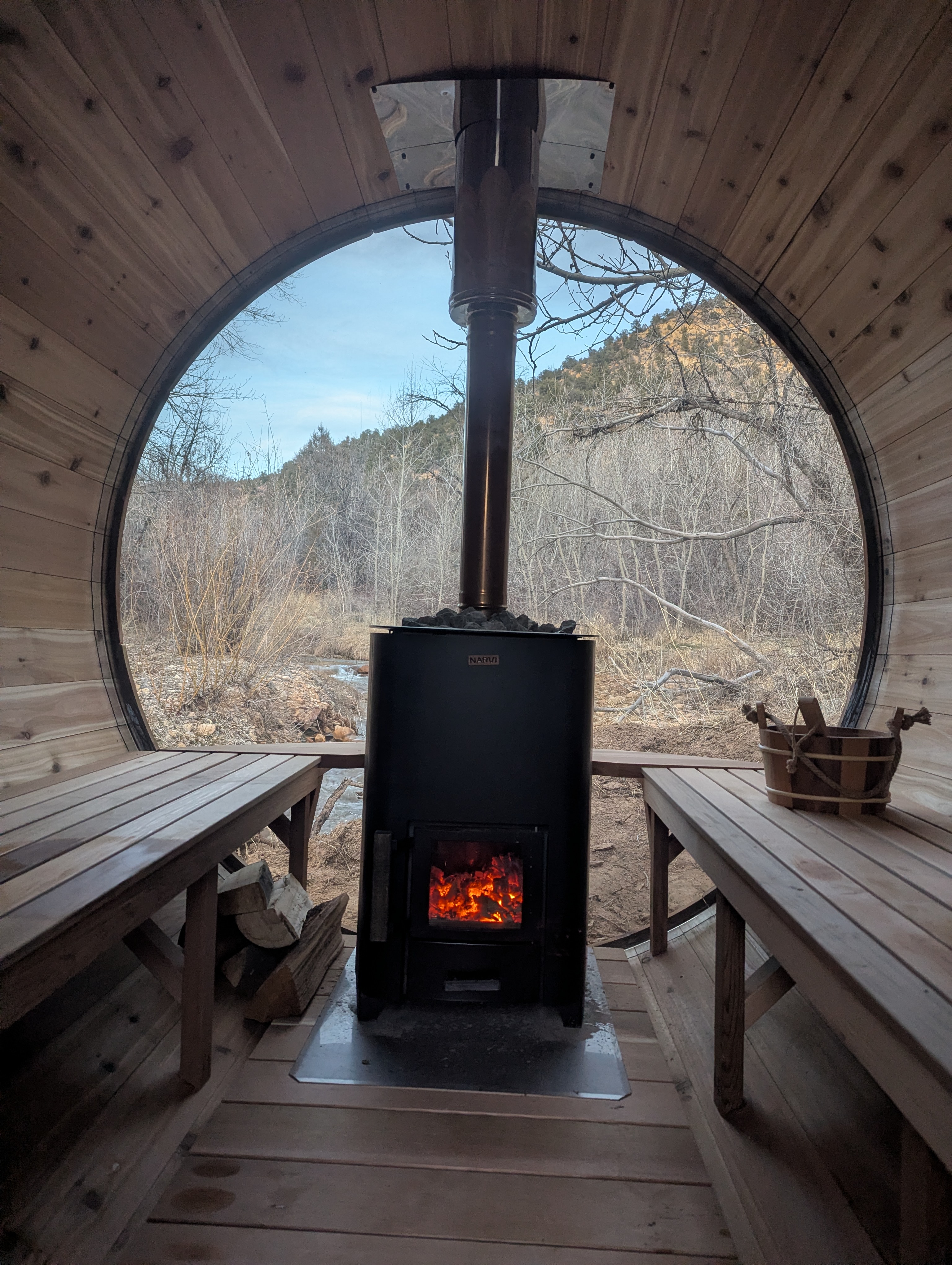 Inside the Zen Zion barrel sauna — wood-fired stove glowing with canyon view through circular window